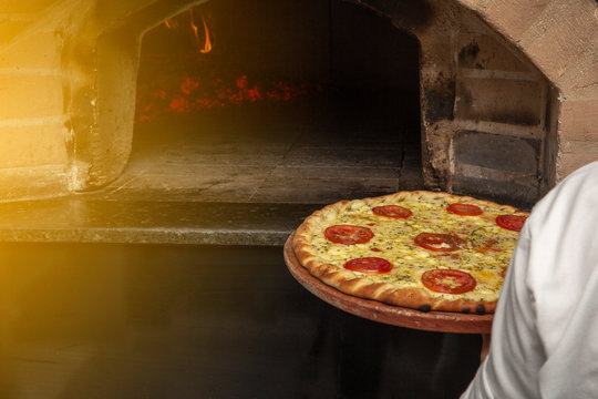 Brazilian pizza is cooked in a wood-fired oven. Pizza cooking in a traditional brick wood oven. Brick oven pizza on the wooden holder going to bake.