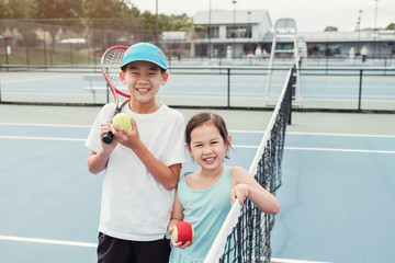 Happy young mixed Asian girl and boy tennis player on outdoor blue court