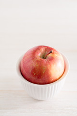 Red apple in a small white bowl