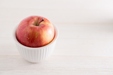 Red apple in a small white bowl