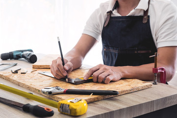 Carpenter working carefully looking at the plans work in carpentry. He is successful entrepreneur at his workplace. hammering a nail Supports On Building Site work with cutter.