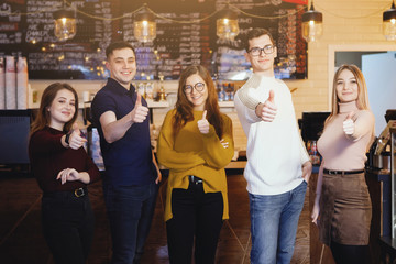 Group of five young men guys and girls are happy to pose for the camera in a cafe.