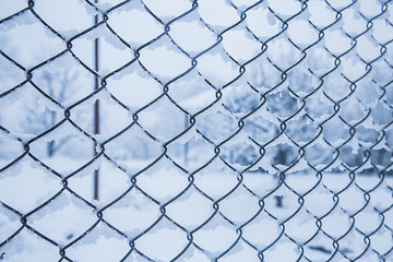 Fototapeta premium Wire fence in the snow. Fence background. Metallic net with snow. Metal net in winter covered with snow. Wire fence closeup. Steel wire mesh fence vintage effect. - Image