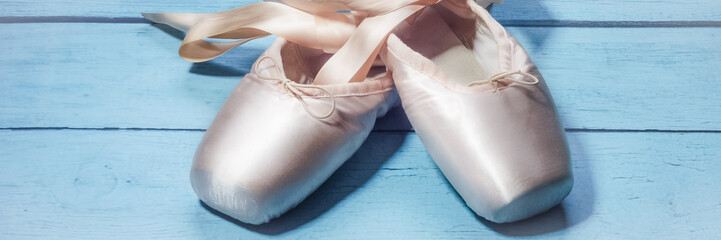 Pointe shoes ballet dance shoes with a bow of ribbons beautifully folded on a wooden background.
