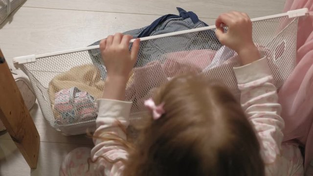 Little girl cleans up clothes in home wardrobe