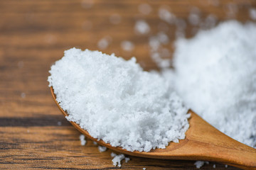 Salt in wooden spoon and heap of white salt background