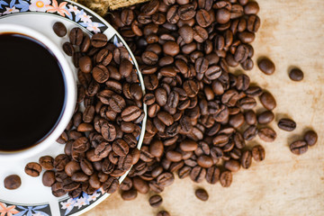 Coffee cup on roasted coffee beans on sack and rustic wood background top view