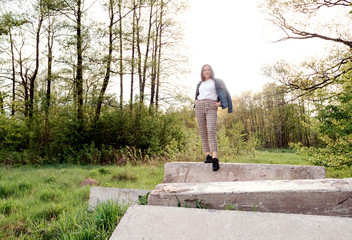 Young girl with long brown hair standing on rock in green summer, spring forest. Place for text.