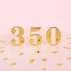 Number 350 in golden numbers on a pink background and golden confetti. Space for text...