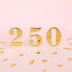 The number 250 is gold numbers on a pink background and golden confetti. Space for text..