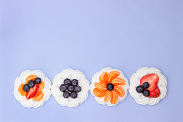 Meringue with blueberries, strawberries and tangerines on a lavender background. Minimal concept. Top view