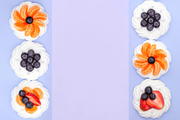 Frame of meringue with blueberries, strawberries and tangerines on a lavender background. Top view