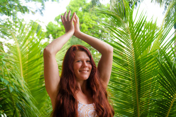 natural portrait of young happy and attractive woman with beautiful long red hair doing yoga meditation exercise at amazing tropical jungle background in healthy lifestyle and harmony