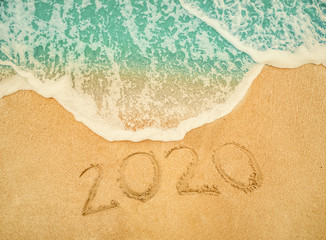 Fototapeta na wymiar Happy New Year 2020 written on seashore sand at sunrise concept.