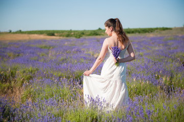 Fototapeta na wymiar adult pretty woman in white summer dress holding lavender bouquet behind her back standing in blooming meadow concept of beauty in nature