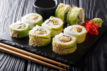 Japanese rolls wrapped in avocado with omelet, sesame and cucumber closeup on a plate. horizontal