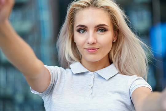 Business woman making selfies in front of office building. Smiling lady taking photos for her business partners abroad.