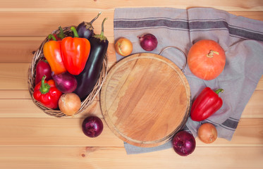 Cutting board with fresh vegetables and napkin on wooden background.