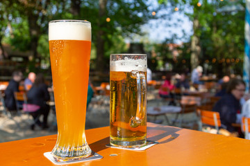 A wheat beer and a pils are standing on a table in a beer garden - obrazy, fototapety, plakaty