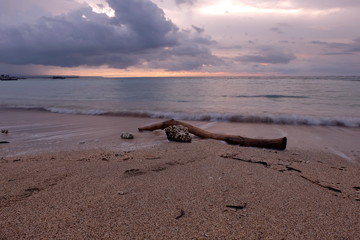 A piece of wood on the sand of Kuta Bali beach which was photographed at dusk, with beautiful sky colors