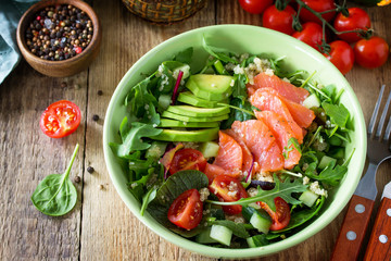 Diet menu, Vegan food. Healthy salad with quinoa, arugula, Tomatoes, Salmon and Avocado on rustic table. Free space for your text.