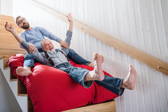 An adult hipster son and senior father indoors at home, having fun.