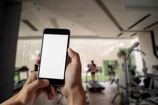 Hand holding white mobile phone with blank white screen  in gym.