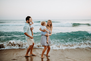 Young family with two toddler children walking on beach on summer holiday.