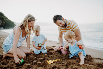 Young family with toddler children playing with sand on beach on summer holiday.