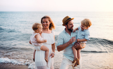 Young family with two toddler children walking on beach on summer holiday.