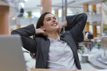 Fototapeta premium Young businesswoman sitting at office desk hold hands behind head relaxing feels good.