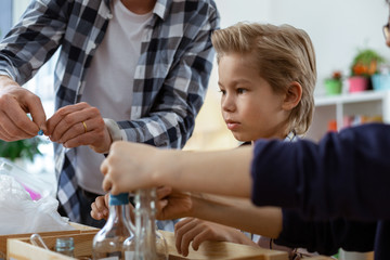 Smiling positive teacher in checkered shirt controlling his young nature lovers
