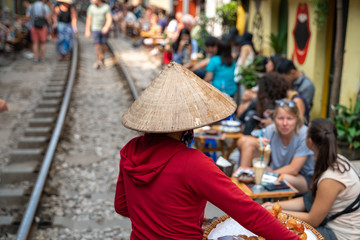 Fototapeta na wymiar Vietnamese woman vendor walking along railroad with people drink coffee or walking on railways waiting for train to arrive on railway road in Hanoi, Vietnam.