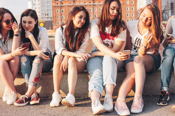 Obraz premium Group of young happy girls real friends students using mobile at city street on sunset background