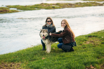 Two female walk with husky dog by the river. Friend with pets