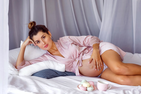 Portrait of beautiful pregnant girl in a home robe resting in bed in the early morning at home.
