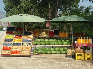 Stargan z owocami i warzywami na sprzedaż, arbuzy, jabłka, śliwki, pomidory, ziemniaki, cytrusy, miód w słoikach i soki domowe w szkalnych butelkach