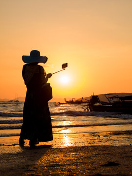 Asian woman taking selfies at the beach at sunset i