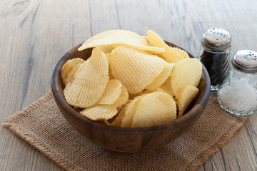 Potato chips in wood bowl  put on the mat with salt and pepper.back natural light food photo concept.