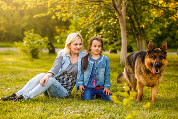 Fototapeta premium Mother and daughter with pet sitting on the grass at the summer park