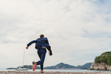 Businessman running to the sea holding in hand briefcase. Back view