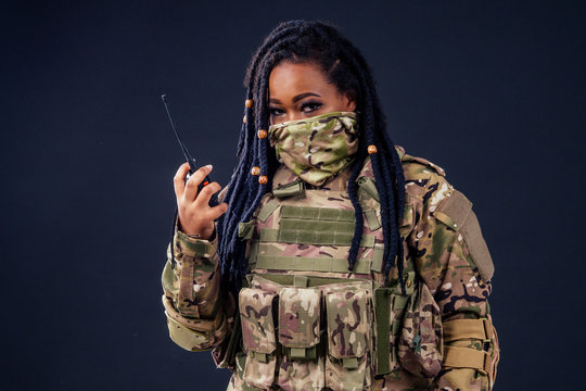 Woman in a military camouflage with a radio afro american army latin soldier in camouflage clothes hair dreadlocks evening makeup on a black background in the studio.