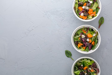 Baked veggies salad with beetroot, carrot and cheese in white bowls on grey background, top view with copy space