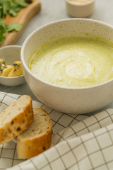 Broccoli cream soup with cheese in a white bowl with bread on the side