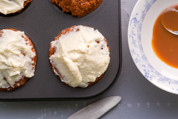 Carrot cupcakes with cream cheese frosting in cupcake tin, close up, top view