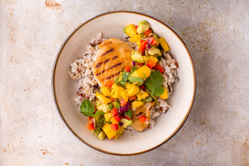 Grilled chicken with mango avocado salsa and rice in a light bowl, top view