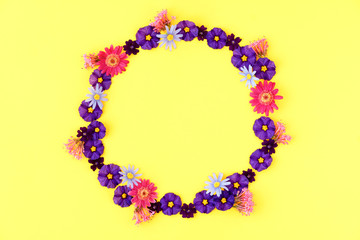 Flowers composition. Wreath made of purple, pink and blue flowers on yellow background. Flat lay, top view
