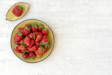 Strawberry in green plate on white wooden background. Top view, copy space