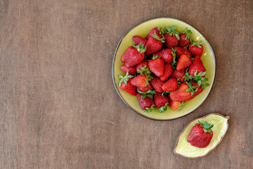 Strawberry in green plate on wooden background. Top view, copy space