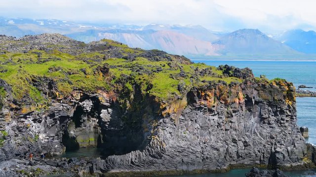 Landscape trail hiking view of rocky beach Valasnos rock cliff in Hellnar national park in Snaefellsnes Peninsula, Iceland with ocean sea waves, green grass in summer with people